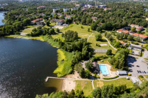 Grönt parkområde vid sjö. I förgrunden brygga och bassäng.